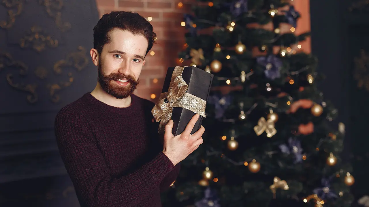 Quoi offrir à son frère pour Noël ? un frère souriant reçoit un cadeau de noël devant un sapin