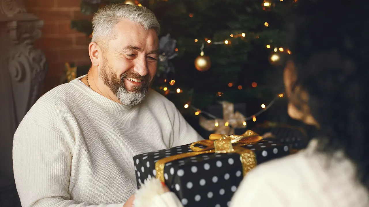 Papa souriant recevant un cadeau de Noël devant le sapin