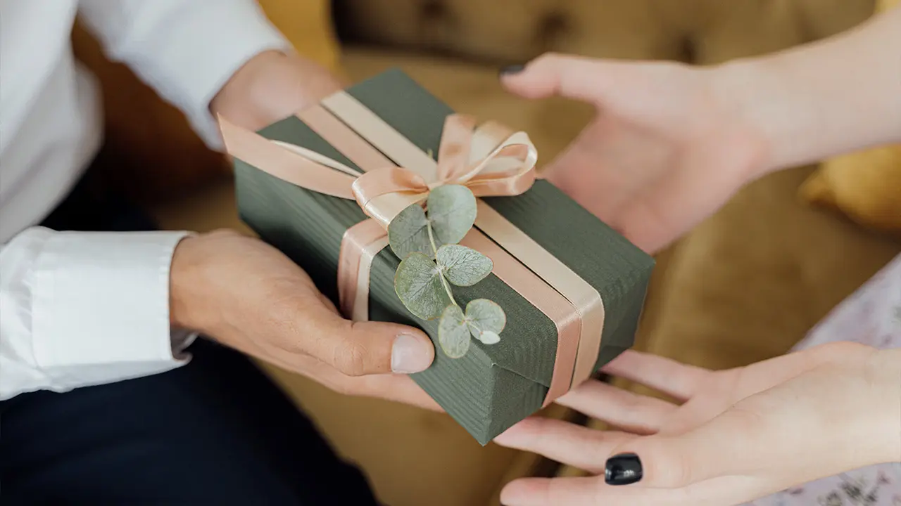 Homme offrant un cadeau vert au ruban pêche et brin d'eucalyptus à une femme